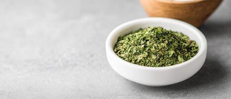 Dried cilantro in white bowl on gray surface, showcasing its vibrant green color and texture, perfect for culinary use photo