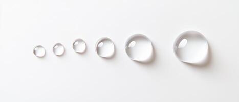 Clear water droplets of varying sizes arranged in line on white background, creating serene and minimalist aesthetic photo