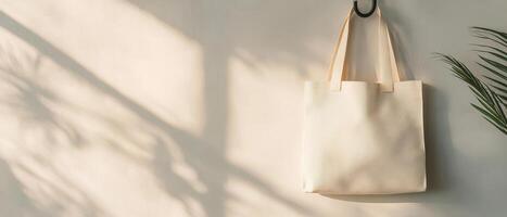 minimalist reusable tote bag hangs against soft wall, casting gentle shadows. serene atmosphere is enhanced by presence of nearby plant, creating calming scene photo