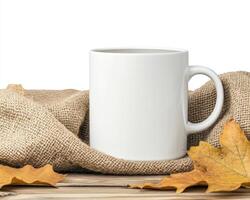 white ceramic mug placed on rustic wooden surface, surrounded by burlap fabric and autumn leaves, creating cozy and warm atmosphere photo