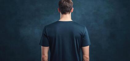 man wearing navy t shirt stands against dark background, showcasing back view of shirt. clean display highlights fabric and color, creating modern and stylish look photo