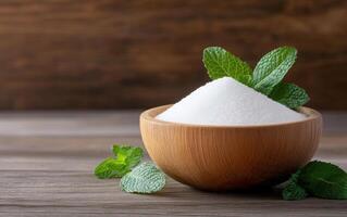 Fresh mint leaves surround bowl of white sugar, creating natural and inviting scene. wooden bowl adds warmth, while mint enhances freshness of composition photo