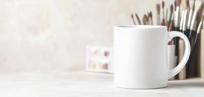 blank white mug sits on table, surrounded by art supplies, evoking sense of creativity and inspiration. Perfect for showcasing your designs or artwork photo