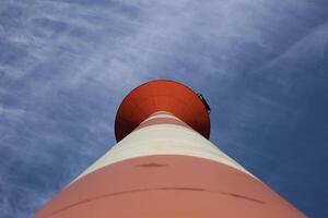 Modern red and white striped lighthouse on blue sky seen from an unusual wide angle directly from below. Rostock, Mecklenburg-Vorpommern, Germany. photo