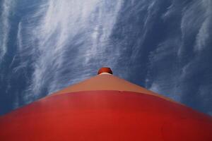 Modern red and white striped lighthouse on blue sky seen from an unusual wide angle directly from below Rostock, Mecklenburg-Vorpommern, Germany photo