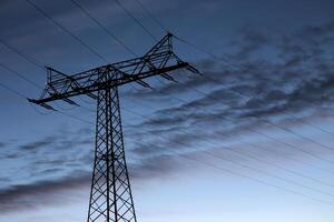 View on a high voltage power line in the evening. The blue sky contains clouds parallel to the power line frame. photo
