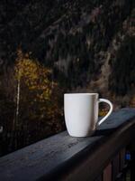 White mug with coffee resting on balcony railing overlooking chamonix mountain view in autumn photo