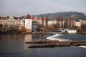 Vltava river flowing through prague with traditional buildings and weir in the foreground photo
