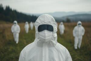 Group of individuals in protective suits walking through a field on a cloudy day near a forested area photo
