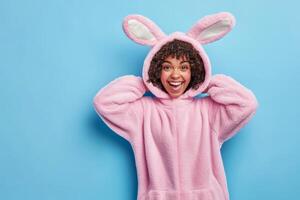 Cheerful individual wearing a pink bunny onesie poses with joy against a light blue background in a playful setting photo