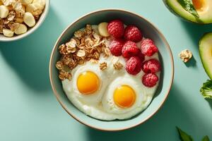 A nutritious breakfast bowl featuring eggs, raspberries, granola, and avocado arranged on a teal background photo