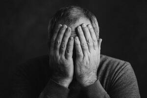 A man covers his face with hands, expressing deep emotion in a monochrome portrait taken indoors during low light photo