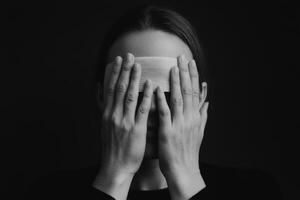A person with covered eyes holding a wooden object in a dark setting, conveying emotions of introspection and contemplation photo