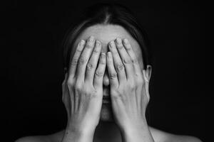 A woman covers her face with her hands in a thoughtful moment against a dark backdrop in a serene indoor setting photo