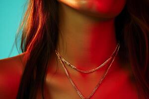 A close-up view of layered gold necklaces worn by a person with long hair illuminated by vibrant red and blue lighting photo