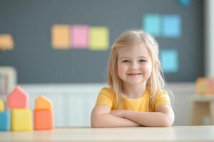 Young girl smiling confidently while sitting at a table with colorful building blocks in a bright classroom setting photo