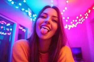 Cheerful young woman with tongue out in colorful room decorated with glowing lights during evening photo