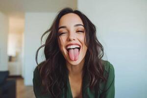 A woman with long hair playfully sticking out her tongue while smiling in a bright, modern living space photo