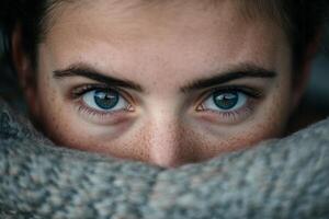 Close-up of a person with striking blue eyes wrapped in a cozy sweater in a warm indoor setting photo