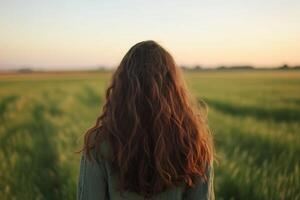 A person with long hair stands in a green field at sunset, enjoying the peaceful landscape and warm glowing light photo