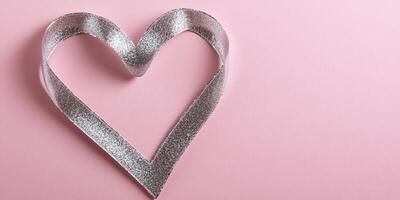 Shimmering silver ribbon heart on soft pink background with romantic theme photo