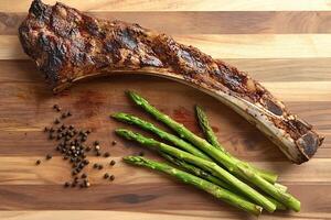 Grilled tomahawk steak with asparagus and black pepper on wooden cutting board photo