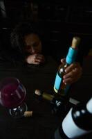 Person reflecting at a table with wine bottles and a glass in view photo
