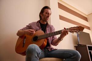 Man playing acoustic guitar in a cozy indoors setting with intent expression photo