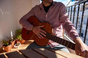 Man sitting with a classical guitar on a sunny balcony patio photo