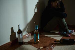Woman sitting on the floor surrounded by multiple empty wine bottles photo