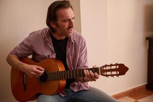Man playing a classic guitar indoors, expressing concentration and passion for music photo