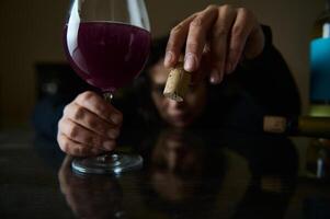 Glass of red wine held by a hand, close-up with cork visible photo