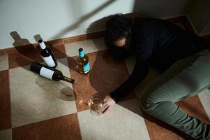 Individual lying on tiled floor surrounded by empty wine bottles photo