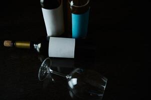 Dark composition of wine bottles with a glass on a reflective surface photo