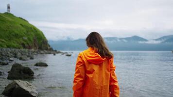 Exploring Unique Location In Kamchatka Peninsula, Woman Tourist In Orange Raincoat Walking On Coast video