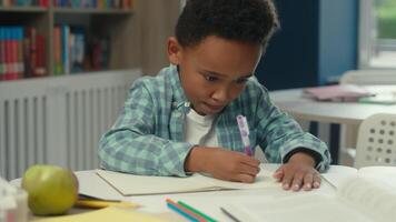 Little boy African American kid son child concentrated studying at school desk elementary primary education writing task class lesson learn write homework student schoolboy studying drawing copybook video