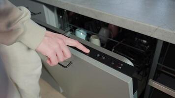 Hand pressing start button on dishwasher control panel with open door. Woman using modern home appliance, choosing automatic program on built in dishwasher for cleaning dirty dishes video