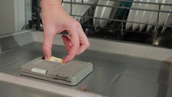 Close-up of hand placing dishwasher detergent tablet into dispenser of open dishwasher with dishes inside. Preparing dishwasher for cleaning cycle. Modern home appliances video