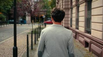 Back view from behind unrecognizable man unknown guy walking outdoors going in city turning around smiling pointing looking at camera hey you smile toothy male portrait tourist outdoor walk at street video