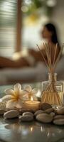 A reed diffuser, candles, and rocks on the table, with frangipani flowers beside them photo