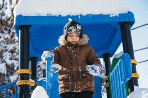 A toddler in a brown jacket and black hat is happily playing in the freezing snow in a public space, enjoying leisure fun in the winter photo