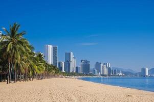 Sandy beach with palm trees by sea in a resort town with skyscrapers in summer in Nha Trang in Vietnam during the day photo
