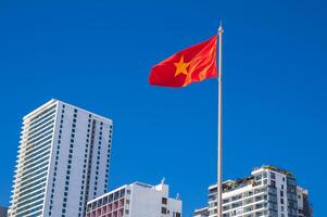 The flag of Vietnam on a flagpole against a background of blue sky and skyscrapers in resort city of Nha Trang in Vietnam photo