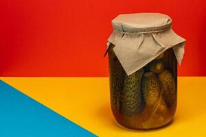 Homemade pickled cucumbers and vegetables in a jar on a colorful background photo