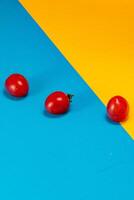 Bright red tomatoes on vibrant blue and yellow background create vivid contrast photo