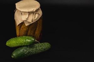 Homemade pickled cucumbers and fresh vegetables on a dark background photo