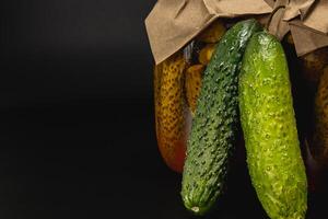Homemade pickled cucumbers and tomatoes in jars on a dark background photo