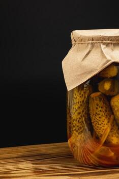 Homemade pickled cucumbers and vegetables stored in jars on wooden surface photo