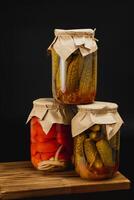 Homemade canned pickles and tomatoes in jars on a wooden surface photo