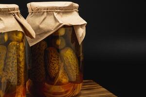 Homemade pickled cucumbers and tomatoes in jars on wooden surface photo